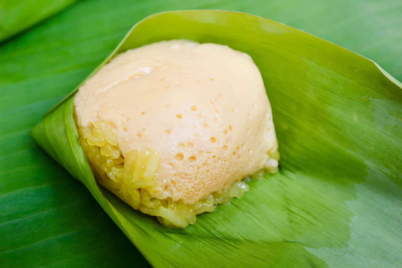 56626401 - thai traditional dessert, sticky rice custard wrapped in banana leaves.